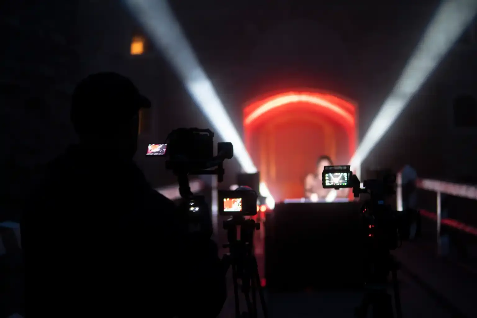 Camera crew filming a DJ set with multiple cameras and dramatic beams of light